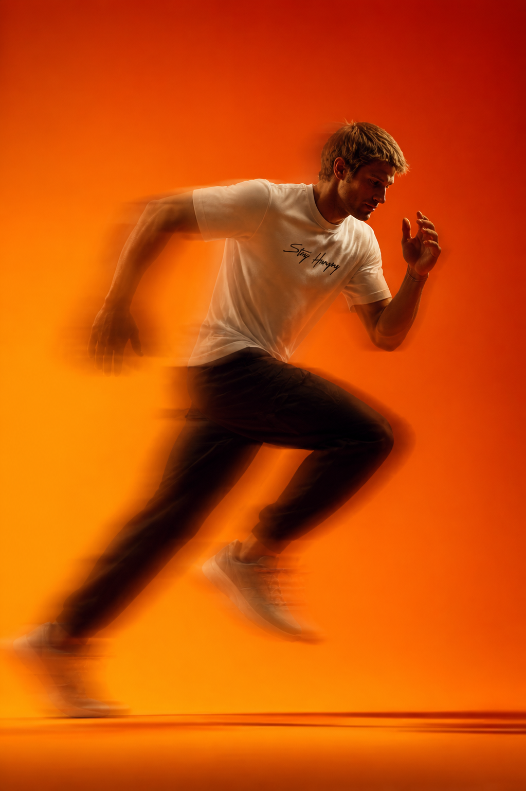 Sprinter mid-stride in a Stay Hungry tee against an orange backdrop