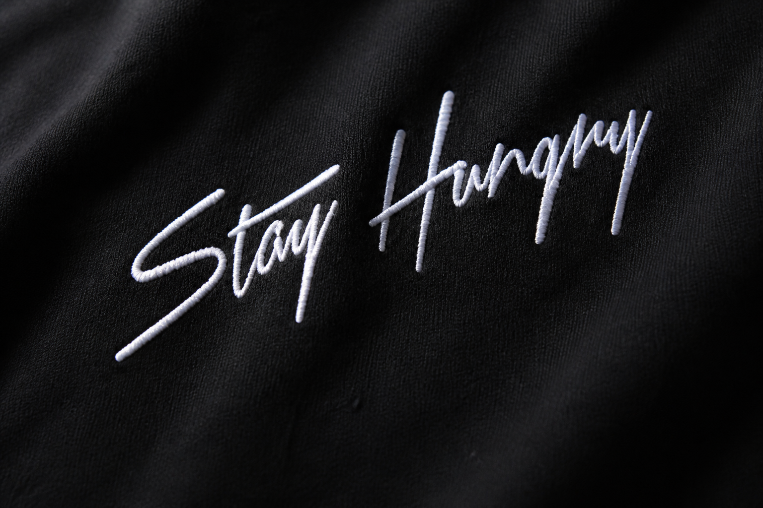 Close-up of the white Stay Hungry embroidered script on black heavyweight cotton