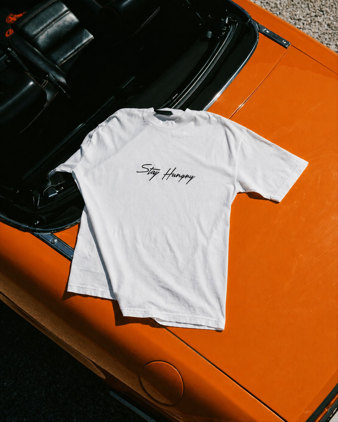 White Stay Hungry tee laid across the hood of an orange sports car
