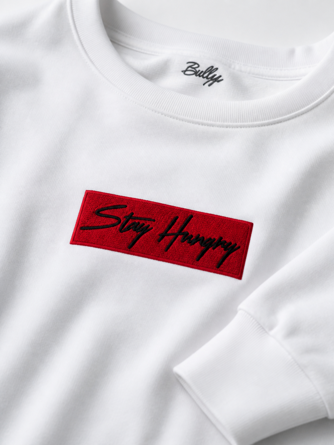 Close-up of the red box Stay Hungry embroidered patch on a white crewneck