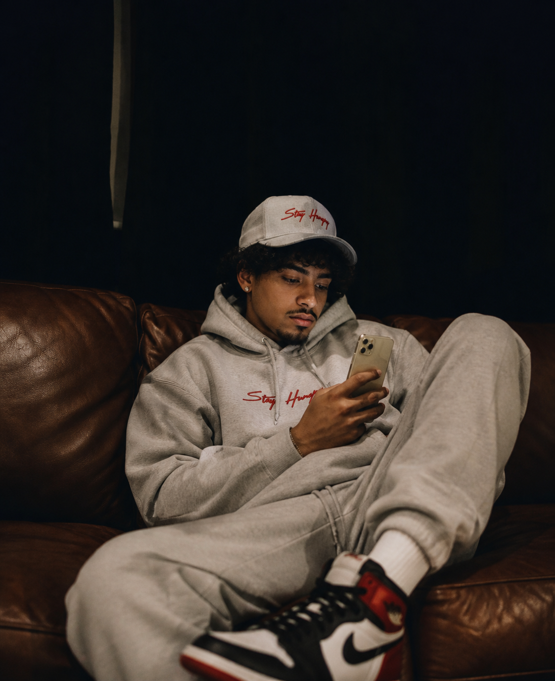 Man in a grey Stay Hungry hoodie and sweats on a leather couch